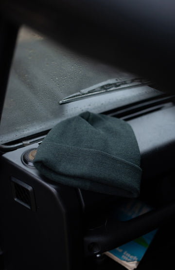 Green wool beanie beanie on a car dashboard with wipers in the background