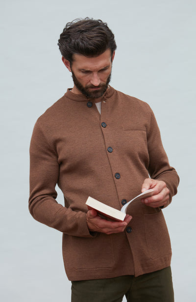 Man wearing a brown mandarin collar jacket in fine wool holding a book against a light gray background