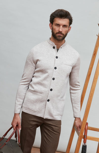 Man wearing a light gray mandarin collar jacket with black buttons against a plain background