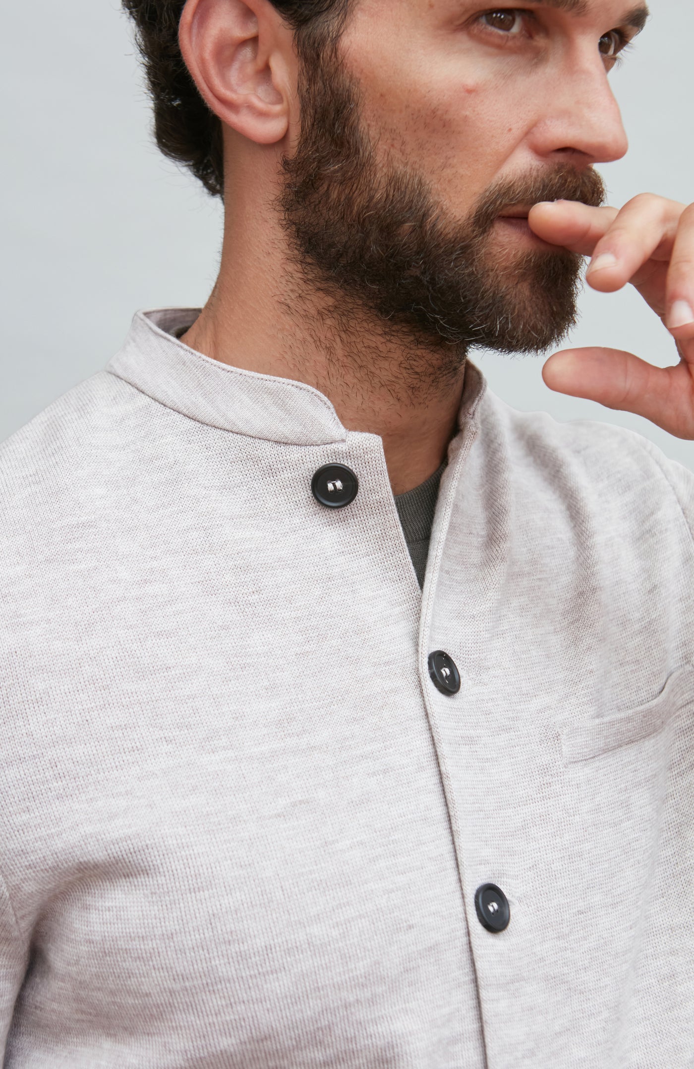 Man wearing a light gray mandarin collar jacke with black buttons on a plain background