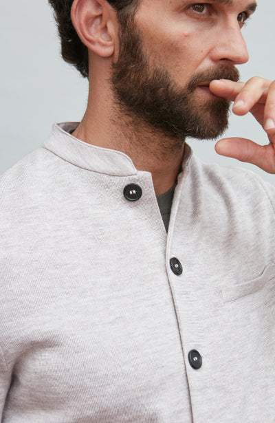 Man wearing a light gray mandarin collar jacke with black buttons on a plain background