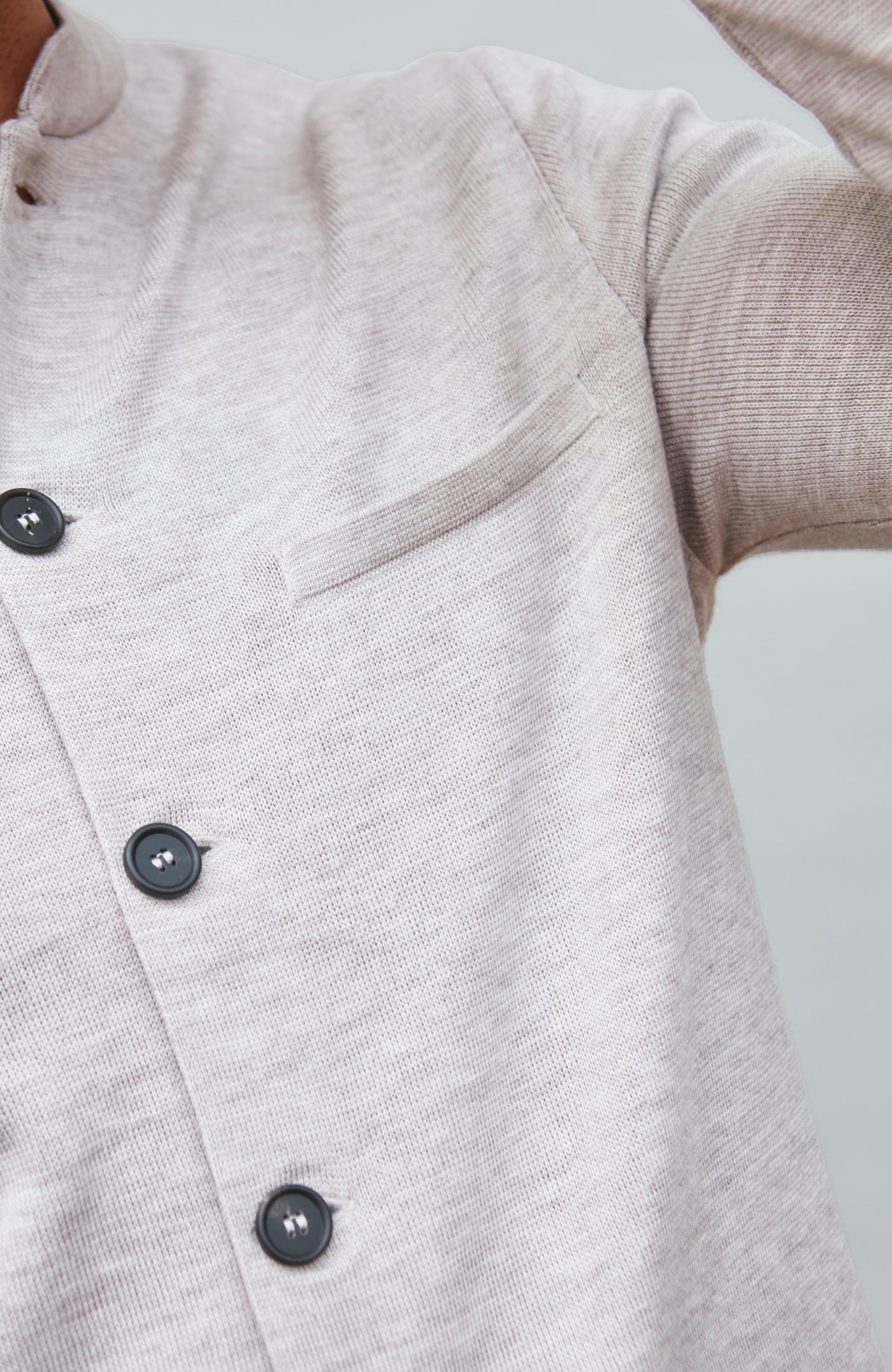 Close-up of a light gray mandarin collar jacke garment with black buttons on a neutral background