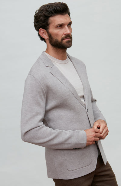 Man wearing a black fine merino wool blazer over a gray shirt with a plain background