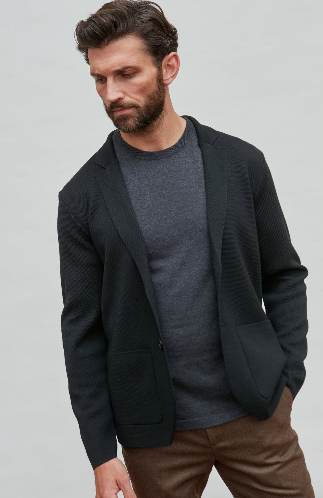 Man wearing a black fine merino wool blazer over a gray shirt with a plain background