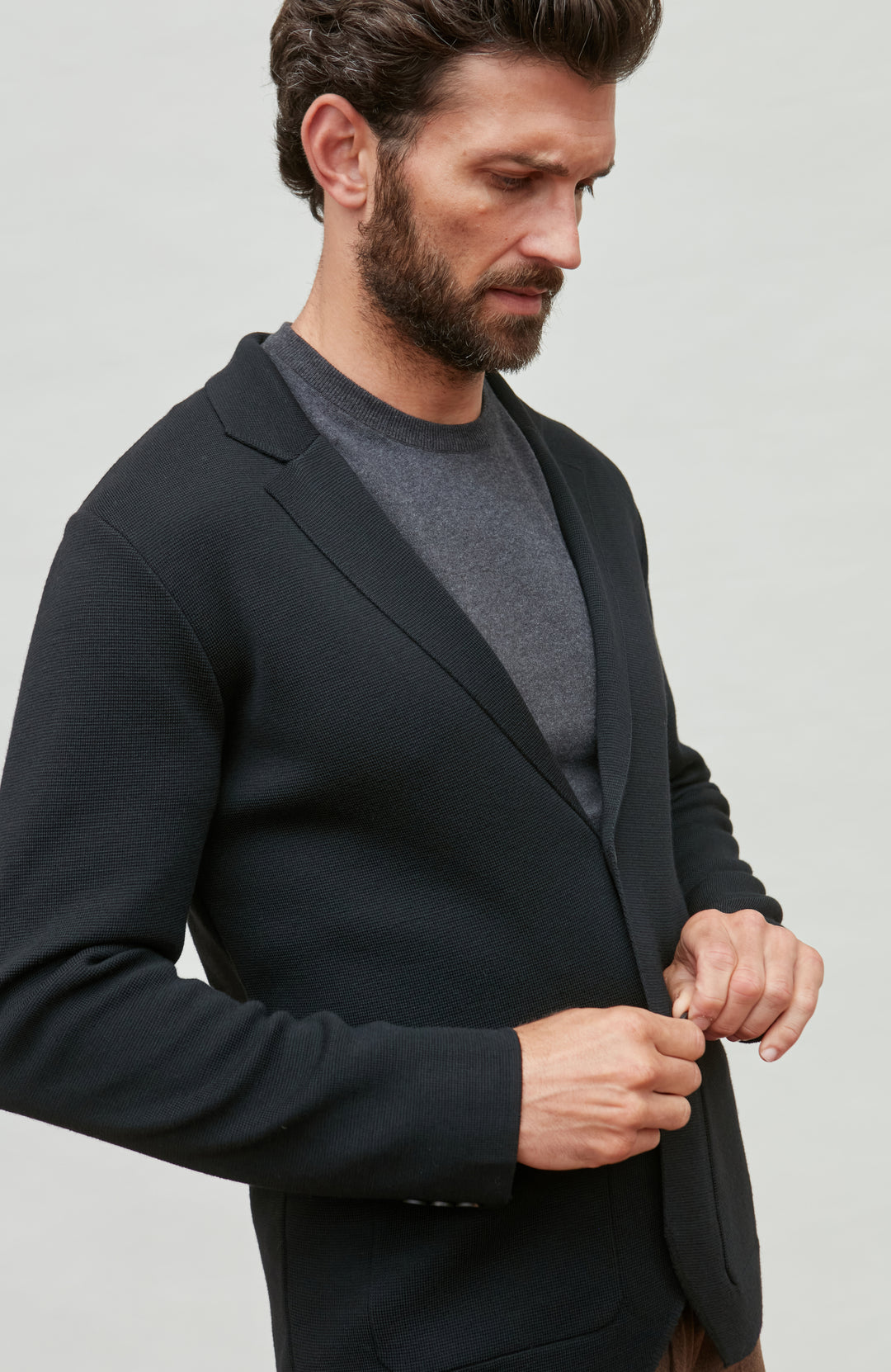 Man wearing a black fine wool blazer over a gray sweater on a light gray background