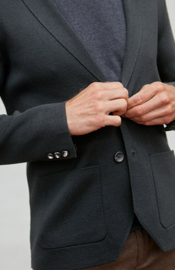 Person buttoning a black wool blazer against a neutral background