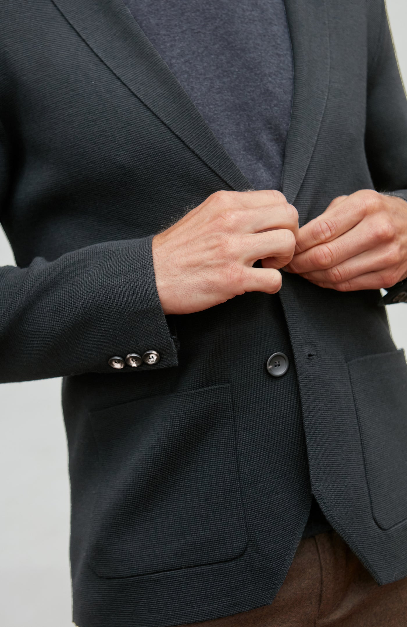Person buttoning a black wool blazer against a neutral background