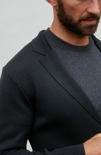 Man wearing a black fine wool blazer over a dark shirt against a plain background