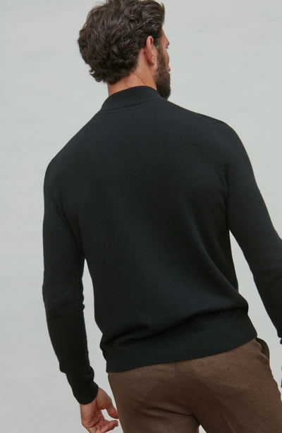 Man wearing a black merino cashmere  sweater and brown pants against a light gray background