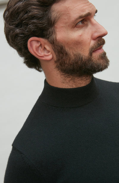 Man wearing a black merino cashmere  turtleneck sweater against a plain background