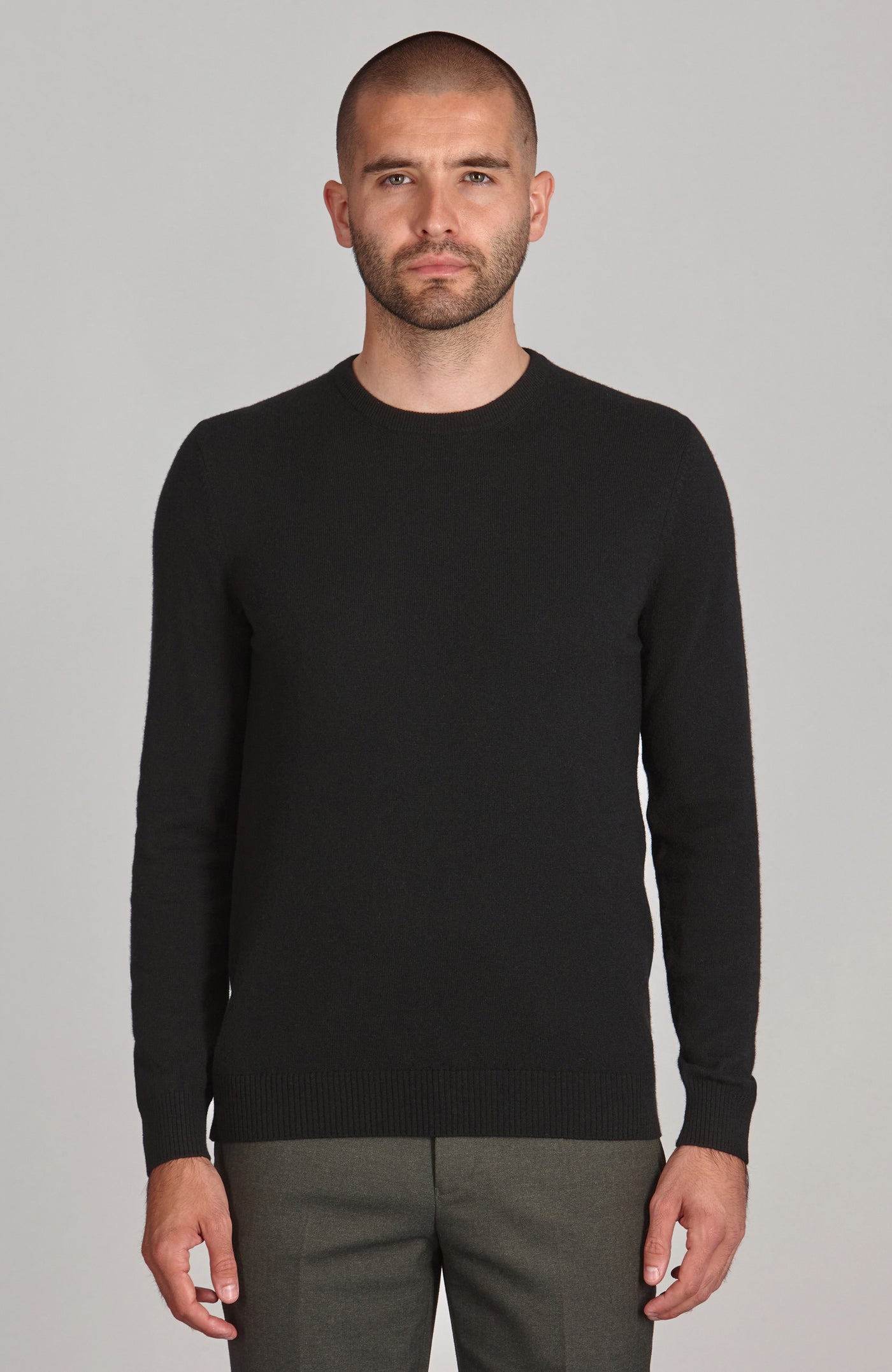 Man wearing a black merino cashmere sweater and gray pants against a gray background