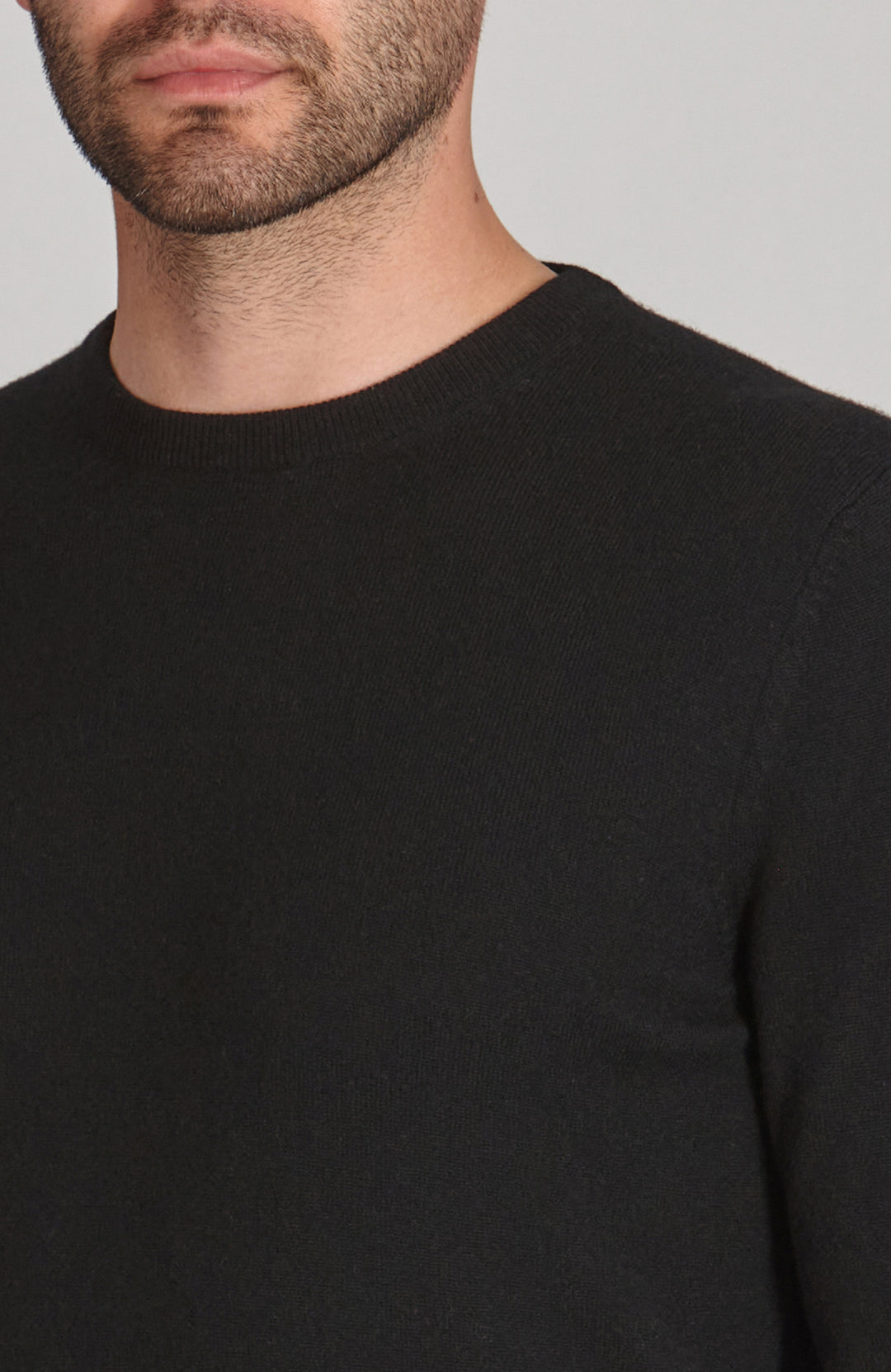 Close-up of a person wearing a black merino cashmere sweater against a neutral background by Paul James