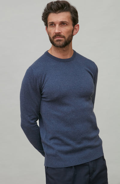 Man wearing a blue merino cashmere  sweater against a gray background
