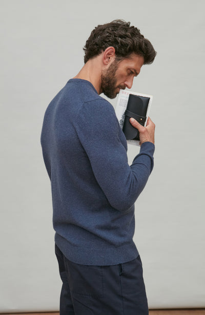 Man in a blue blue merino cashmere holding a black phone against a plain background