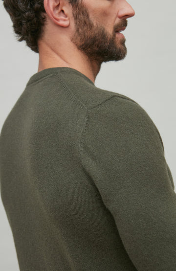 Man wearing a green merino cashmere sweater against a plain background by Paul James