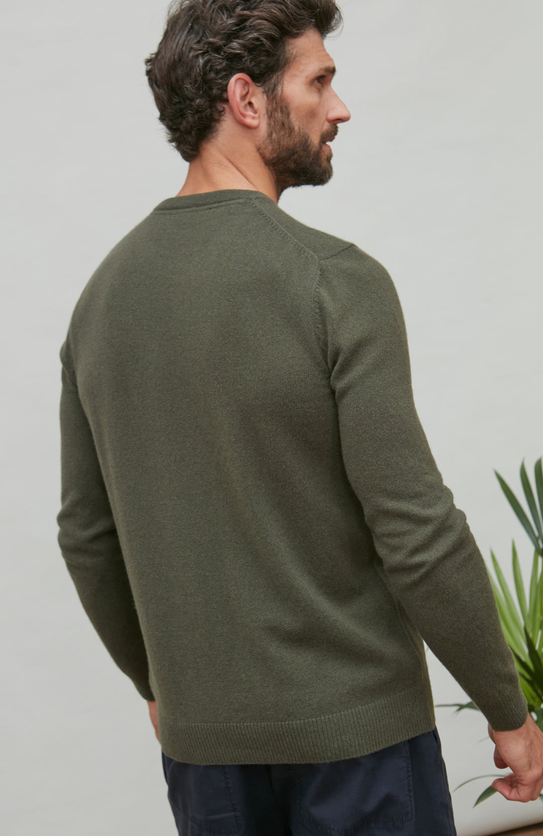 Man wearing a green merino cashmere crew neck sweater against a plain background by Paul James