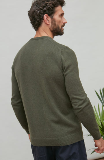 Man wearing a green merino cashmere crew neck sweater against a plain background by Paul James