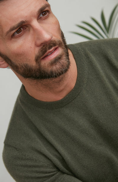 Man wearing a green merino cashmere sweater with a neutral background
