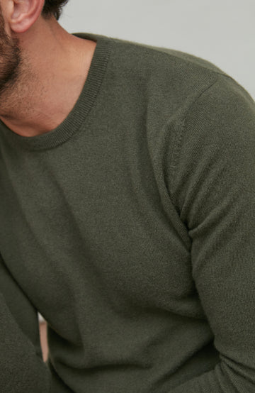 Close-up of a person wearing a green merino cashmere sweater against a neutral background by Paul James