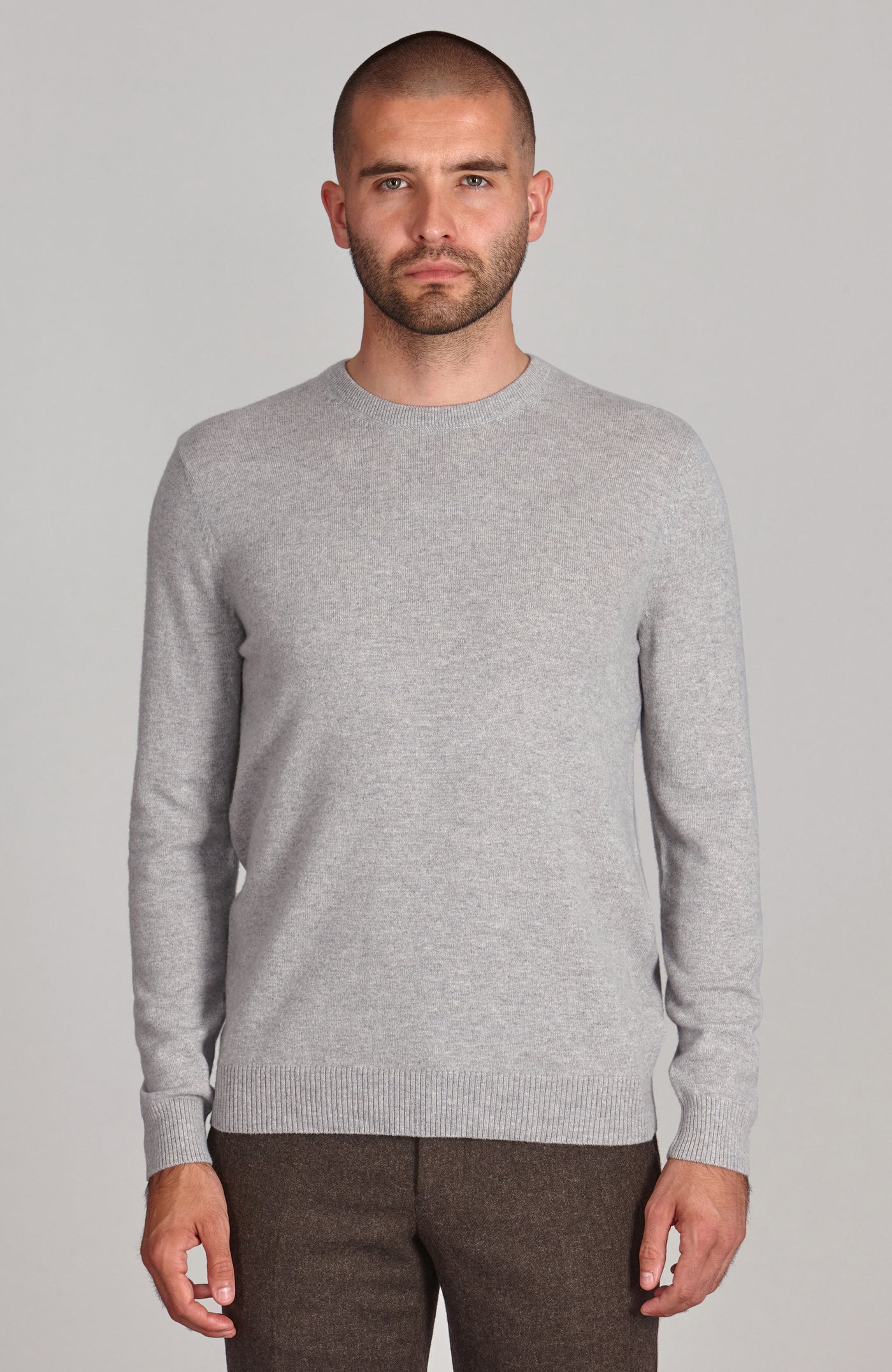 Man wearing a gray merino cashmere crew neck sweater against a plain background