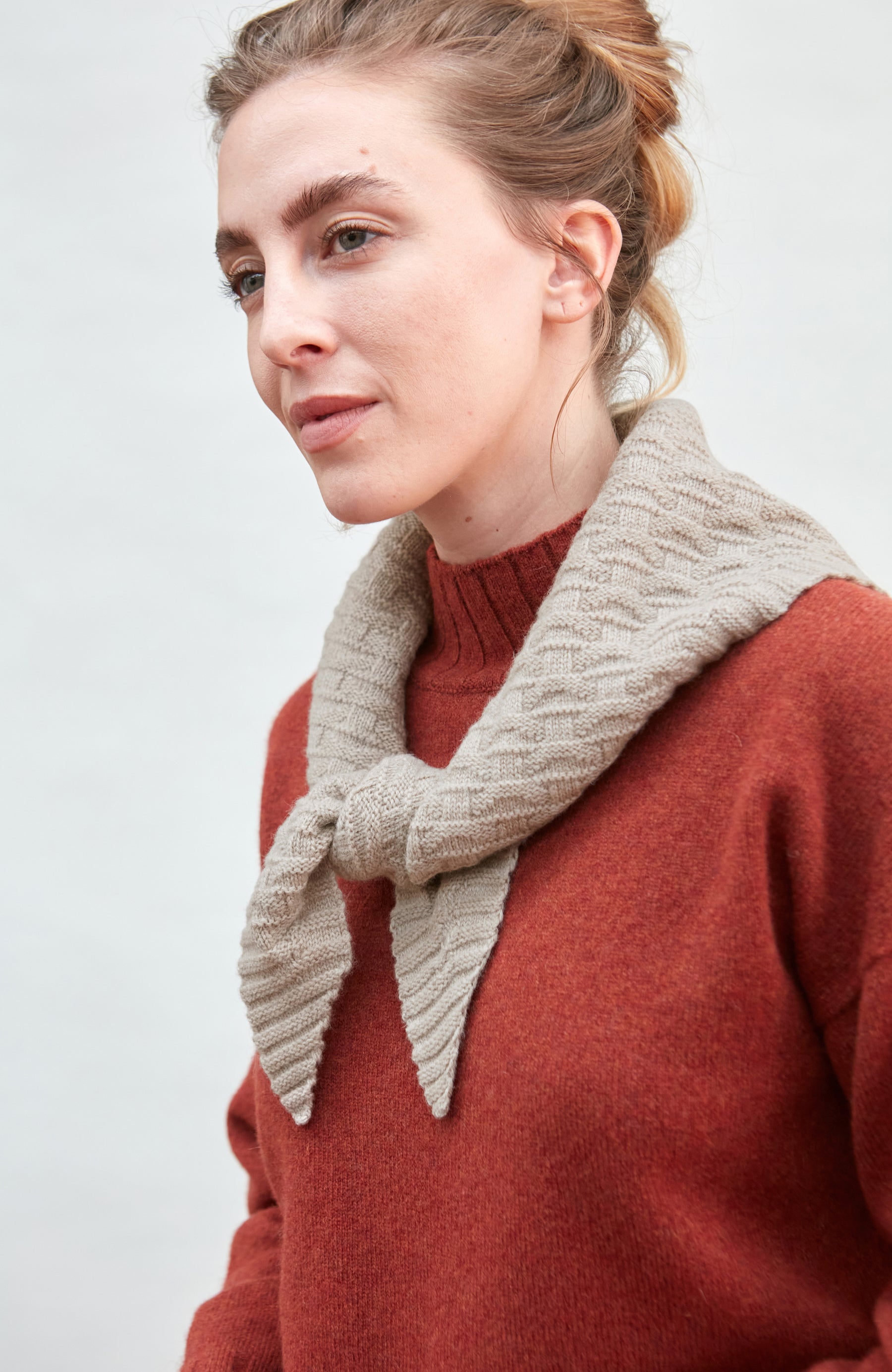 Woman wearing a beige knitted beige merino cashere knitted neckerchief  and red sweater on a plain background by Paul James 