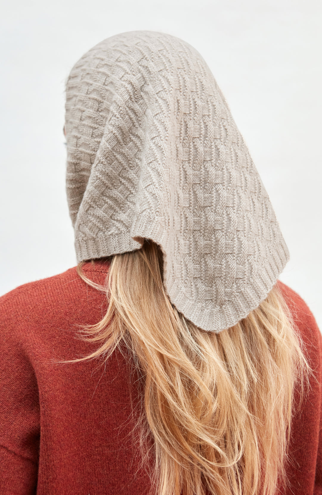Person wearing a textured beige merino cashmere knitted headscarf on a white background by Paul James