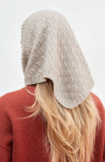 Person wearing a textured beige merino cashmere knitted headscarf on a white background by Paul James