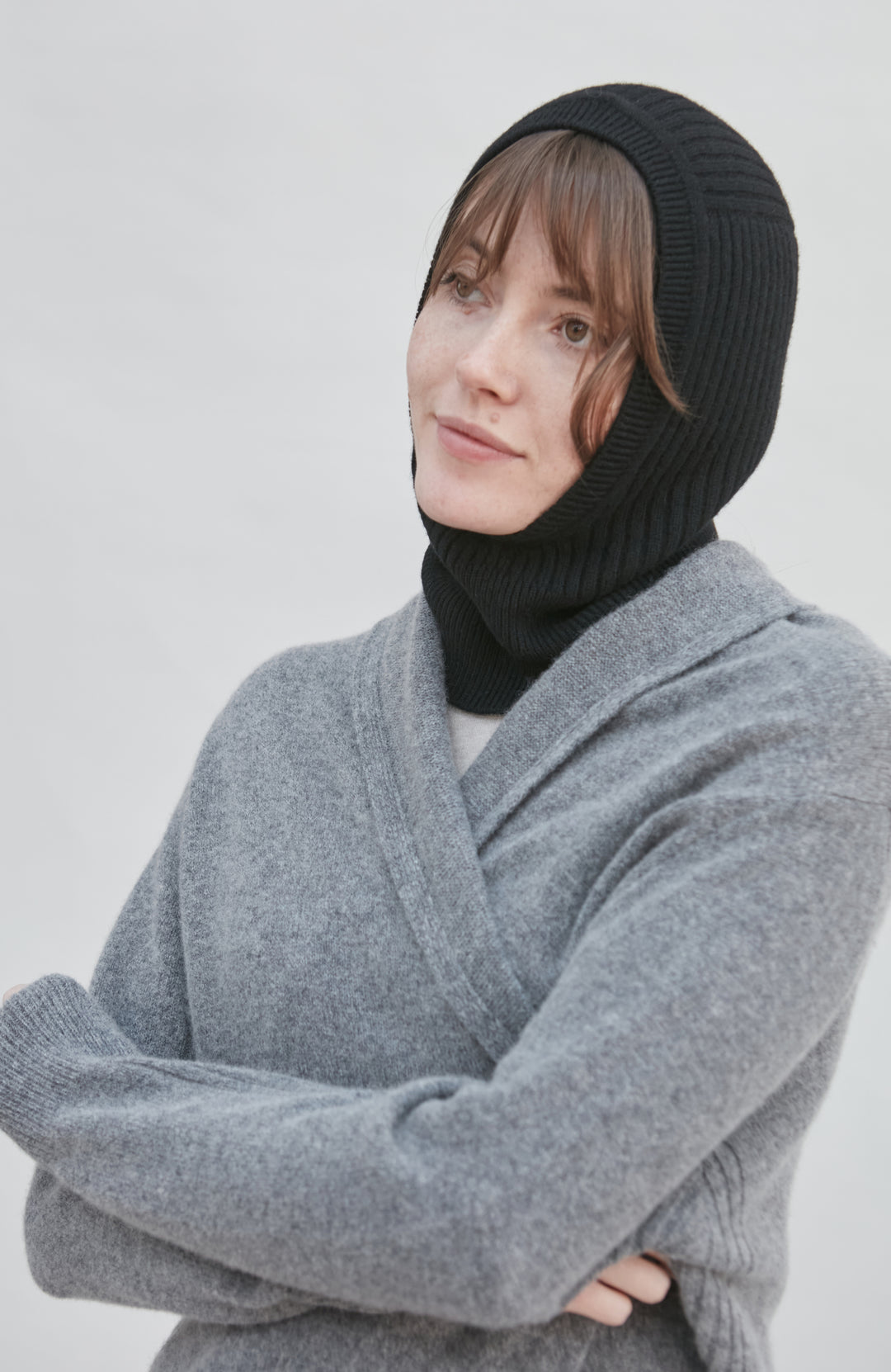 Person wearing a black knit merino cashmere balaclava and gray sweater against a white background by Paul James