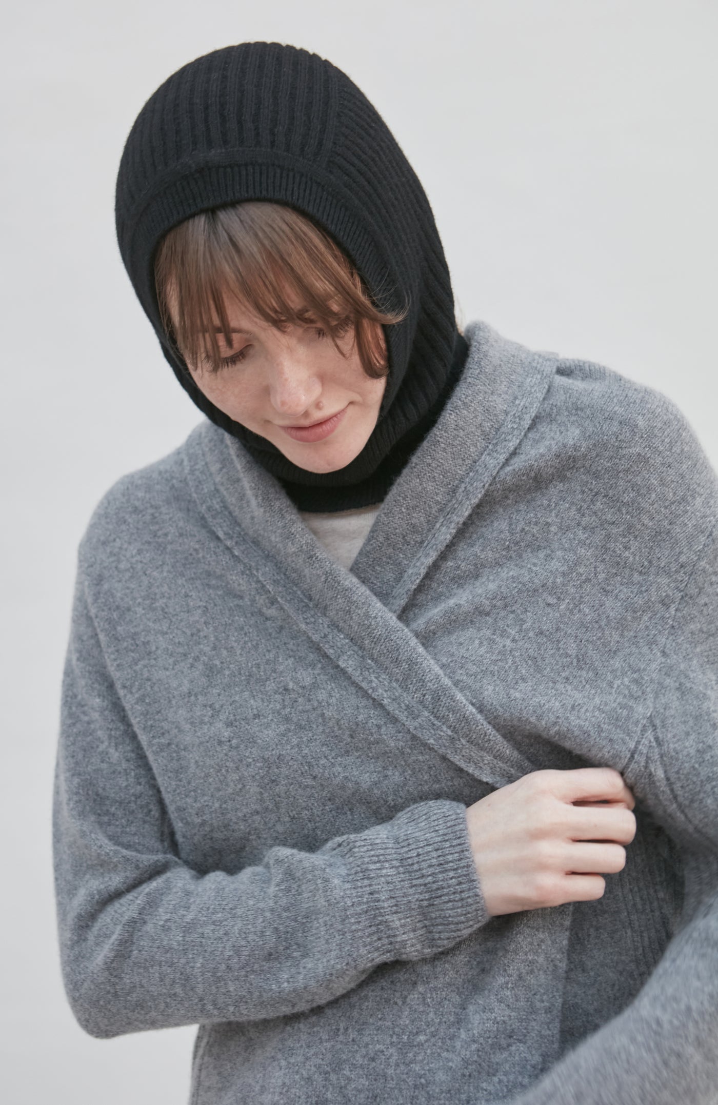 woman wearing a gray wrap, black balaclava, and black scarf against a light background